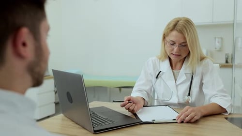 Doctor Woman Sitting in Medical Office Speaking with Man Patient During Consultation