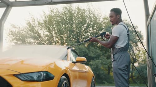 Man Washing a Yellow Car with Water