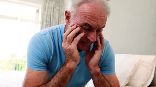 Tense senior man sitting on bed in bedroom