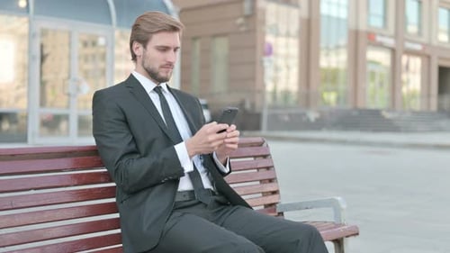 Man in Suit Uses Smartphone on Bench