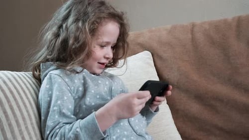 Cute Girl Engrossed in Smartphone on Comfortable Sofa