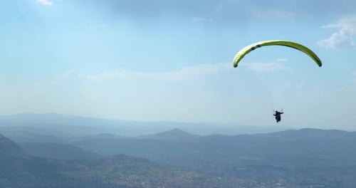 Paraglider Soaring Over Mountains and Distant City