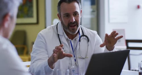 Caucasian male doctor using laptop sitting and addressing hospital colleagues at a meeting