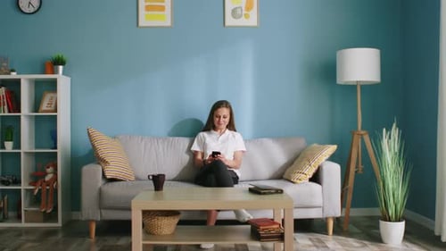 Woman Using Smartphone on Sofa in Cozy Living Room