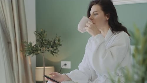 Woman in Robe Drinking and Using Mobile Phone