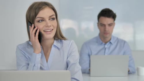 Woman Speaking on Phone at Laptop in Office