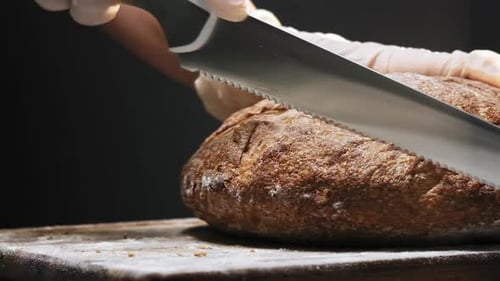 Hands Slicing Crusty Brown Bread with Knife