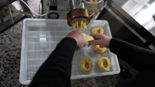 Closeup male hands preparing fresh spaghetti noodles using machine inside pasta factory