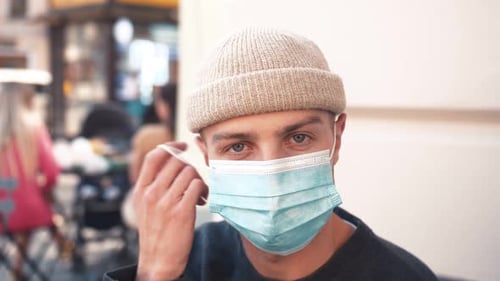 Close Up of Face of Young Handsome Caucasian Man Taking Off Medical Mask at Cafe. Looking Straight