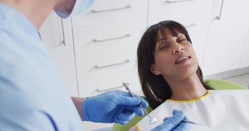 Kaukasischer männlicher Zahnarzt mit Gesichtsmaske, der die Zähne einer Patientin in einer modernen Zahnklinik untersucht
