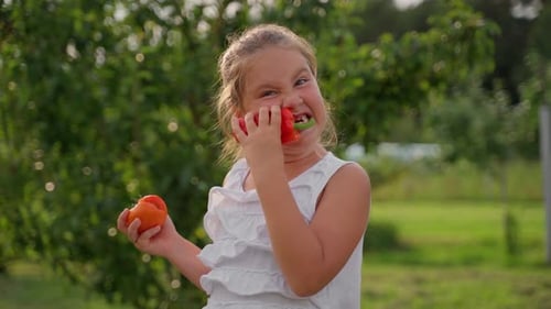 Portrait cute girl biting vegetable pepper at garden. Young school aged child person lick vegetables