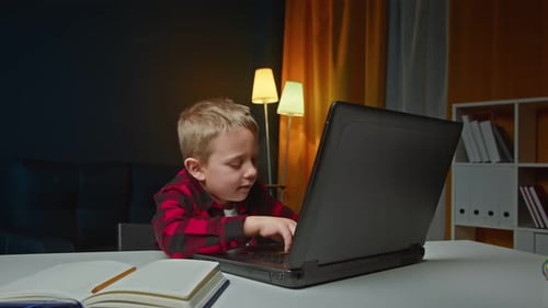 Child Uses Laptop at Table Indoors at Night