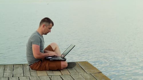 Full side view of smiling mature man using laptop on pier