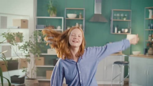 Red Haired Woman Joyfully Dancing in Modern Kitchen