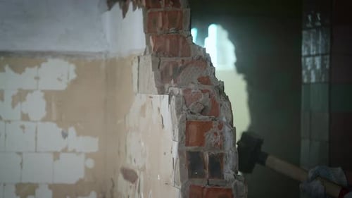 A Worker with a Sledgehammer Demolishes a Brick Wall