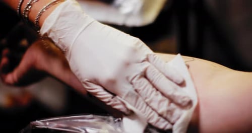 Tattoo artist sprinkles sterile liquid on a person's hand with a tattoo. BMPCC 4K