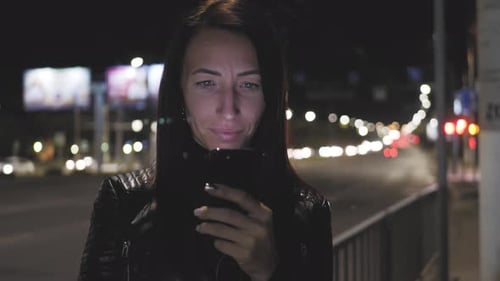 Close Up Woman Using Smartphone in the City at Night Time. Girl Looks at the Smartphone Screen