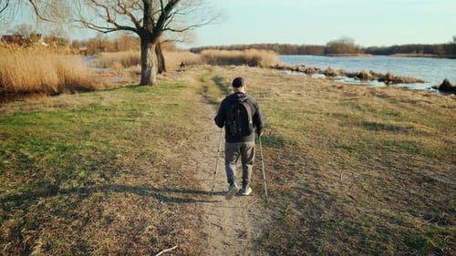 Active Handsome Elderly Man with Nordic Walking Sticks Walks Forward Through Along the Lake at