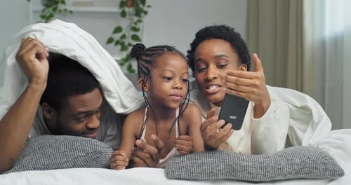 Happy Family Using Smartphone Together in Bed