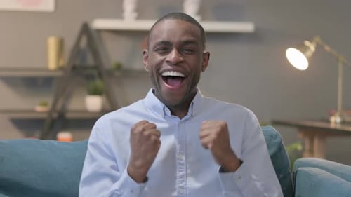Excited Young Adult Cheers Indoors on Sofa