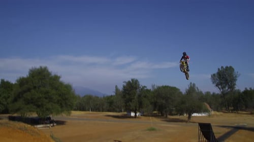 Dirt Bike Rider Jumping Ramp in Rural Setting