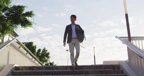 Asian man with backpack walking down the stairs at corporate park