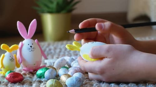 Une fille dessine un motif sur un œuf de Pâques en forme de lapin avec des œufs de Pâques en arrière-plan