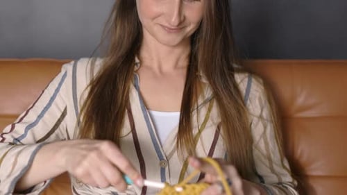 Young Smiling Woman Crocheting with Knit Needles at Home, Close Up