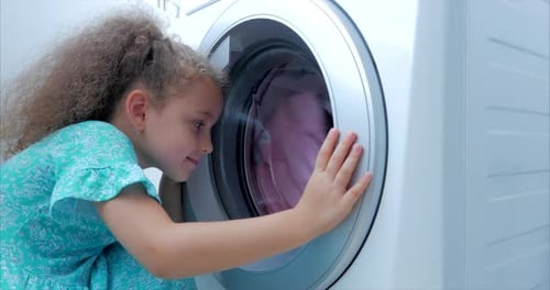 Süßes Kind schaut in die Waschmaschine. Zylinder-Spinnmaschine. Concept Wäschewaschen