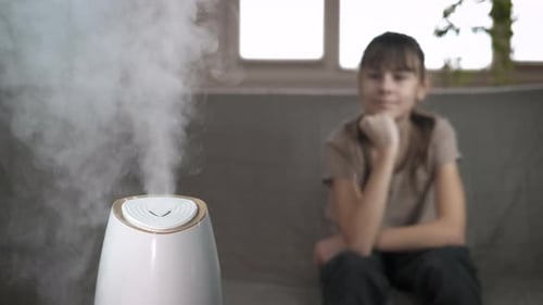 White Humidifier Emitting Vapor with Child in Background