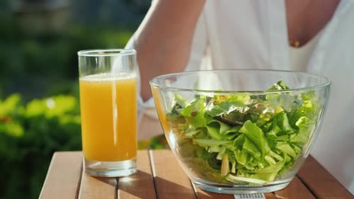 Woman Eating Salad and Drinking Orange Juice Outdoors