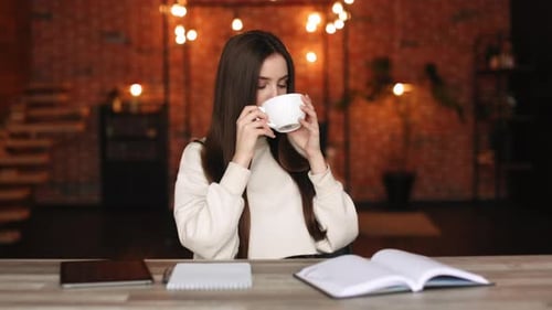 A Woman is Sitting in Her Home Office and Drinking Tea