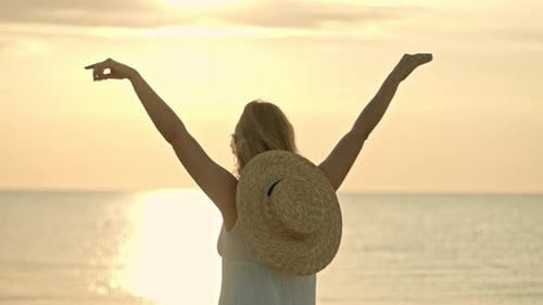 Woman in White Dress and Straw Hat Standing with Open Arms on Sea Beach. Beauty, Nature, Travel