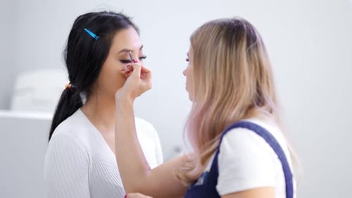 Maquiadora profissional fazendo maquiagem para sobrancelhas de modelo feminina usando lápis Medium Shot