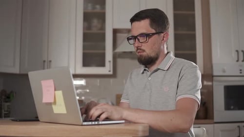 Tired Man Is Typing on a Laptop, Sitting in Home, Taking Out His Glasses