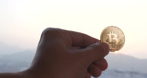 Hand Holding Bitcoin Cryptocurrency Coin at Sunrise
