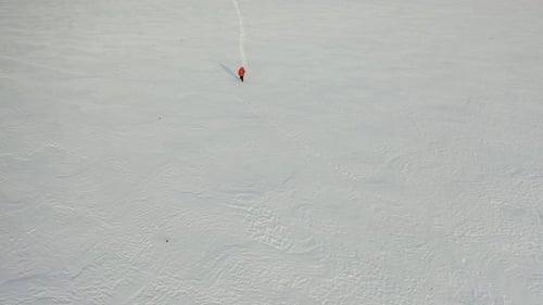 Aerial Footage a Man with a Backpack and Sticks Walks Through the Snowy Desert Leaving a Chain of