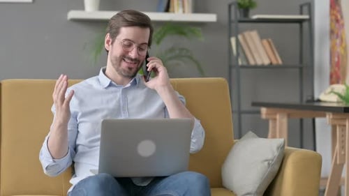 Happy Man Talking on Phone While Using Laptop