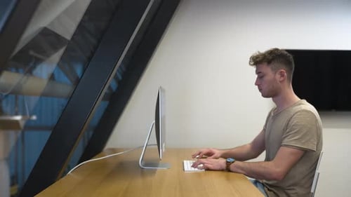 Young man in profile,casual dresscode,working on PC in a modern office.