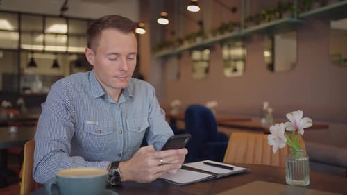 Medium Shot of Young Man Wearing Streetwear Sitting in Restaurant or Cafe in Front of Laptop and