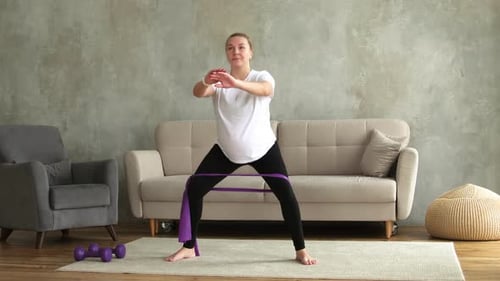 Woman Exercising with Resistance Band Doing Squats at Home