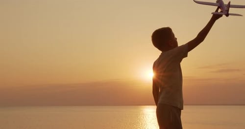 Child Playing with Toy Airplane at Beach Sunset