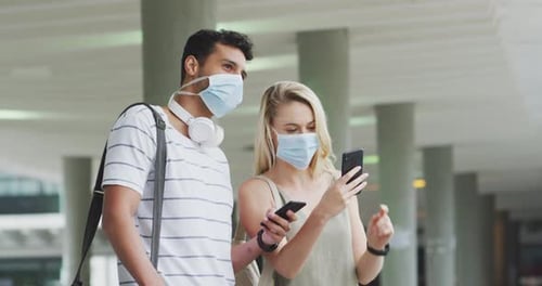 Side view of Caucasian couple on the go wearing a coronavirus covid19 mask and using phone
