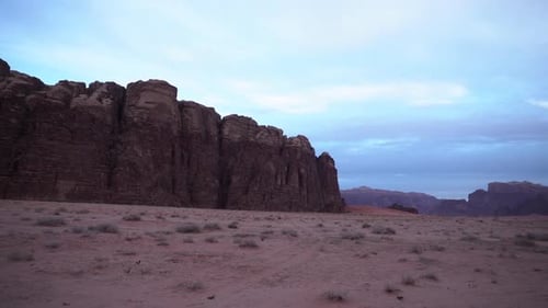 A Panoramic Shot Of Wadi Rum Desert Canyon With Sand, Mountains And White Clouds In The Background