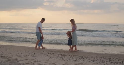 Young Parents Play with Their Children Near the Water at the Sea Coast