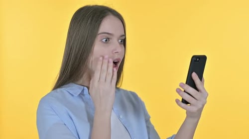 Surprised Woman Interacts with Smartphone on Yellow Background