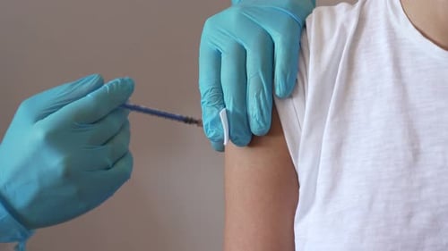 Closeup Woman and Her Doctor Wearing Face Masks and Getting a Vaccine Shot in a Doctor's Office