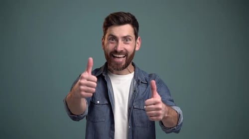 Freudig überraschter bärtiger Mann, der Daumen hoch zeigt, wie eine Geste, in die Kamera schaut