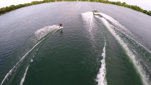 Aerial birds-eye drone view of a man wakeboarding behind a boat.