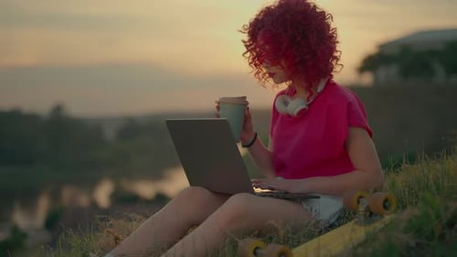 Woman Works on Laptop at Sunset with Skateboard